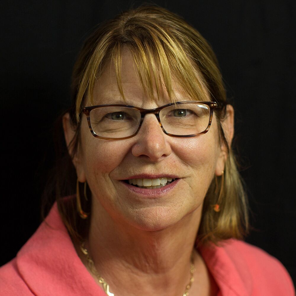 A woman with glasses, short blonde hair, and a pink top smiles warmly, embodying the spirit of local home care services.