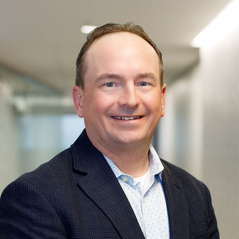 A man in a dark blazer and light shirt smiles while standing in a well-lit hallway, highlighting the professionalism often associated with personal care services.