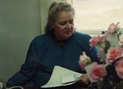 A person sits by a window holding papers, with a vase of pink roses in the foreground, representing personal care services.