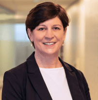 A woman with short brown hair is smiling while wearing a black blazer and white shirt in an indoor, well-lit setting, reflecting her dedicated role in home health care service.
