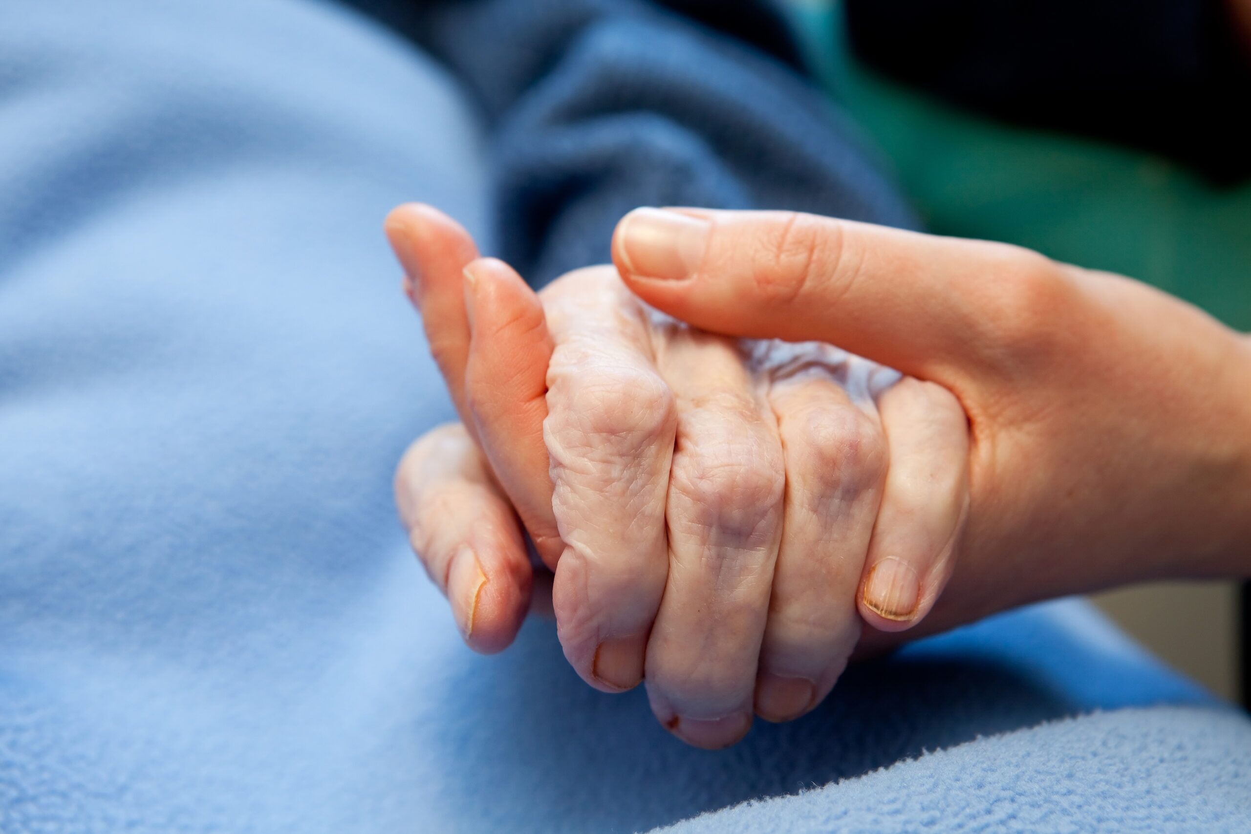 A younger person holds the hand of an older person resting