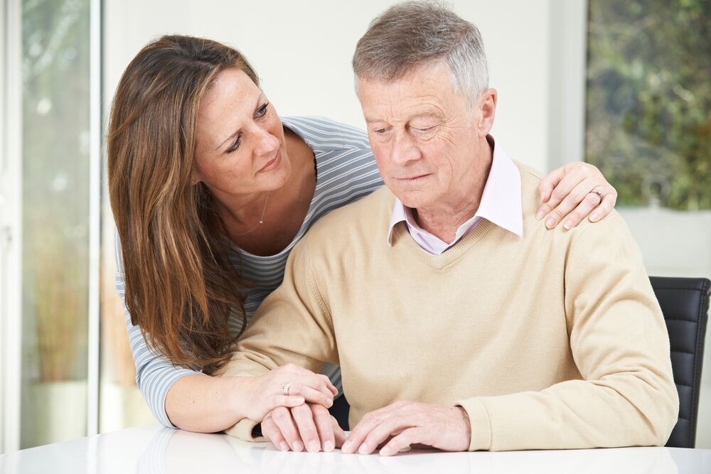 A woman places a comforting hand on the shoulder of an elderly man